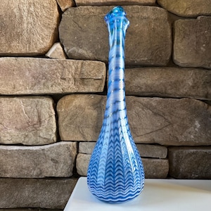 May include: A tall, blue glass vase with a slender neck and a bulbous base. The vase features a pattern of wavy lines and zigzags in shades of blue and white. The vase is approximately 15 inches tall.