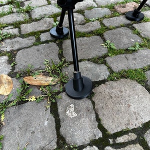 Könnte beinhalten: Nahaufnahme eines schwarzen Metall-Stuhlbeins mit einem Gummifuß, der auf einem Kopfsteinpflaster liegt. Das Stuhlbein gehört zu einem Klappstuhl.