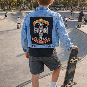 Puede incluir: Chaqueta vaquera azul claro con un parche negro grande con el logotipo de Guns N' Roses y las palabras "Appetite for Destruction". La chaqueta la lleva una persona que sostiene una patineta en un parque de patinaje.