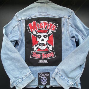 May include: Light blue denim jacket with a large black patch featuring the Misfits logo, a skull, and the words "New Jersey." A smaller patch with the Misfits skull logo is sewn on the bottom. The jacket is a classic style.