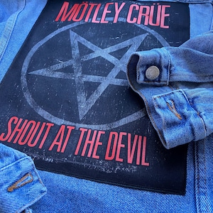 May include: A light blue denim jacket featuring a large rectangular black patch on the back. The patch displays the red text MÖTLEY CRÜE above a distressed white pentagram inside a circle, with the red text SHOUT AT THE DEVIL printed below.