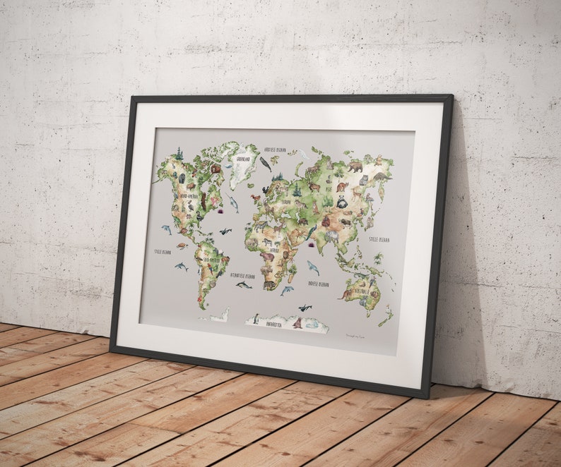Op de afbeelding: Ingelijste wereldkaart kunstprint met een aquarel illustratie van de continenten en oceanen. De kaart bevat dier illustraties en labels. De print zit in een zwart frame en leunt tegen een witte muur en een houten vloer.