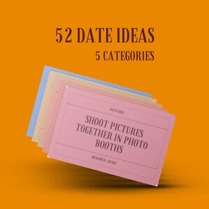 May include: A pink card with the text "52 DATE IDEAS 5 CATEGORIES" at the top and "DATE IDEE SHOOT PICTURES TOGETHER IN PHOTO BOOTHS DRAUSSEN/SPASS" at the bottom. The card is part of a stack of cards with different colours.