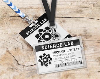 May include: A white plastic ID badge with a black atom symbol and the text "SCIENCE LAB" on the top. The badge has the name "MICHAEL I. KOZAK", address "3106 DAWSON DRIVE LOUISVILLE, KY 40299", and the title "SCIENTIST". The badge is attached to a black lanyard with a silver clip.