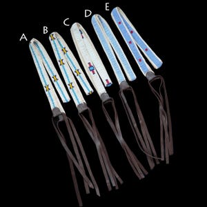 May include: Five beaded leather straps with fringe. The straps are white with blue, red, and yellow bead patterns. The straps are labeled A through E.
