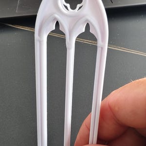 Könnte beinhalten: Ein weißer Fensterrahmen im gotischen Stil mit drei vertikalen Stäben und einem Vierpass-Design oben. Der Rahmen wird in einer Hand gehalten, im Hintergrund ist ein Laptop zu sehen. Dieser Artikel ist wahrscheinlich für Bastelarbeiten oder Dekoration.