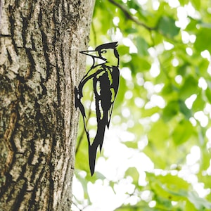 Könnte beinhalten: Schwarze Metallsilhouette eines Spechts, der auf einem Baumstamm sitzt. Die Silhouette ist detailliert und realistisch, mit den Federn und dem Schnabel des Vogels deutlich sichtbar.