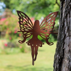 Puede incluir: Una silueta de hada de metal oxidado con alas en forma de mariposa. El hada está unida a un tronco de árbol.