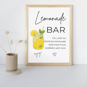 Könnte beinhalten: Gerahmter Druck mit hellem Holzrahmen. Der Druck zeigt die Worte "Lemonade BAR" in einer stilvollen Schriftart, zusammen mit Anweisungen und einer Grafik eines Limonadengetränks in einem Einmachglas. Das Wort "enjoy!" ist kursiv geschrieben.