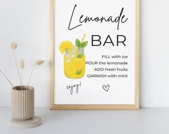 May include: A framed print with a light wood frame. The print features the words "Lemonade BAR" in a stylish font, along with instructions and a graphic of a lemonade drink in a mason jar. The word "enjoy!" is written in cursive.