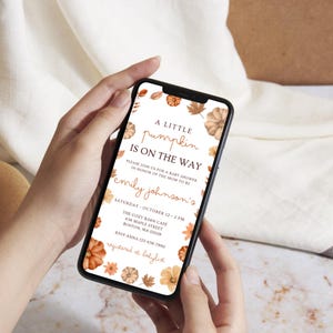 May include: A smartphone displays a baby shower invitation. The invitation features the text "A Little Pumpkin Is On The Way" with floral and leaf accents in orange and brown. The invitation includes the name "Emily Johnson's" and event details.