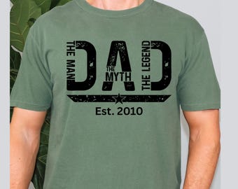 May include: A green t-shirt with a black graphic that reads "DAD" with "THE MAN", "THE MYTH", and "THE LEGEND" text. Below the word "DAD" is a star and the text "Est. 2010".