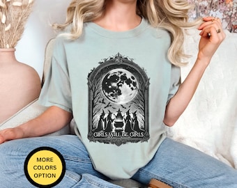 May include: A light blue t-shirt with a black and white graphic of a full moon and four witches standing around a cauldron. The text "Girls Will Be Girls" is printed below the graphic.
