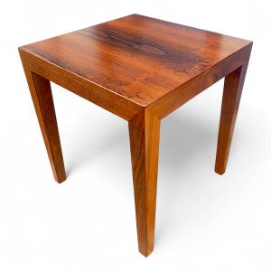 May include: A square, wooden side table with a rich, reddish-brown finish. The table has a smooth top and four angled legs. The wood grain is visible, adding texture and character to the piece. The table measures approximately 20 inches in height and width.