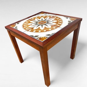 May include: Square wooden side table with a tiled top featuring a circular, geometric design in shades of brown, white, and gray. The table has a dark wood frame and legs, and measures approximately 20 inches square.