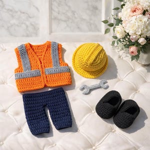 Pode incluir: Um conjunto de crochê para bebé de trabalhador da construção, incluindo um colete laranja e cinzento, calças azul marinho, um capacete amarelo, uma chave inglesa cinzenta e sapatos pretos. Feito à mão.