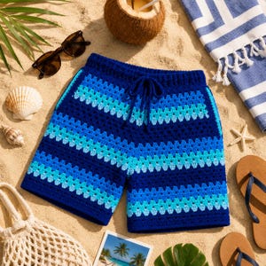 Può includere: Pantaloncini blu all'uncinetto con vita con coulisse, con strisce orizzontali in varie tonalità di blu e turchese. I pantaloncini sono esposti su una superficie sabbiosa, insieme a occhiali da sole, una noce di cocco e accessori da spiaggia.