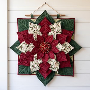 Op de afbeelding: Een gewatteerde wandhanger met een gelaagd kerststerontwerp met dieprode en crèmekleurige stoffen bloemblaadjes. De crèmekleurige bloemblaadjes hebben een print van hulstbladeren en bessen. Het midden is versierd met kleine rode bolletjes.