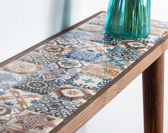 Peut inclure: Une console en bois avec un plateau en carrelage. Les carreaux sont un mélange de bleu, blanc et marron avec des motifs complexes. La table a un design simple avec deux pieds.