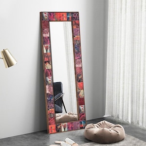 Può includere: Specchio rettangolare a figura intera con cornice in stile mosaico. La cornice è composta da piccoli quadrati colorati con motivi floreali e astratti nei toni del rosso, rosa e viola. Lo specchio è appoggiato a una parete bianca.