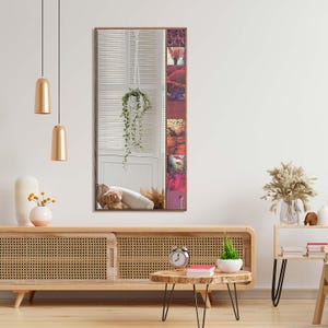 May include: A rectangular mirror with a brown frame. The mirror reflects a room with a window, a hanging plant, and a teddy bear. The right side of the frame has a vertical collage of colorful images.