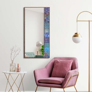 May include: A rectangular wall mirror with a brown frame and a decorative mosaic border in shades of blue, teal, and gold. The mirror reflects a room with a pink armchair and a white side table.