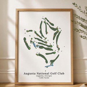 May include: A framed print of the Augusta National Golf Club course layout. The artwork features a green and blue course design on a white background, with the text "Augusta National Golf Club, Augusta, Georgia, 7,445 Yards". The frame is made of light brown wood.