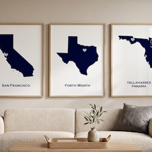 May include: Three framed wall art prints featuring dark blue silhouettes of California, Texas, and Florida. Each state map includes a small light blue heart icon marking a specific location, with the text San Francisco, Forth Worth, and Tallahassee Panama.