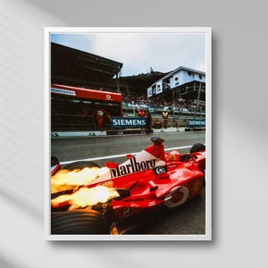 May include: A framed photograph of a red Formula 1 race car with the Marlboro logo, flames shooting from the exhaust. The car is on a racetrack, with a crowd and the Siemens logo visible in the background.