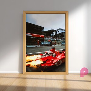 May include: Framed print of a red Formula 1 race car with the Marlboro logo, flames emitting from the exhaust. The car is on a racetrack with the Siemens logo visible. The image is in a wooden frame.