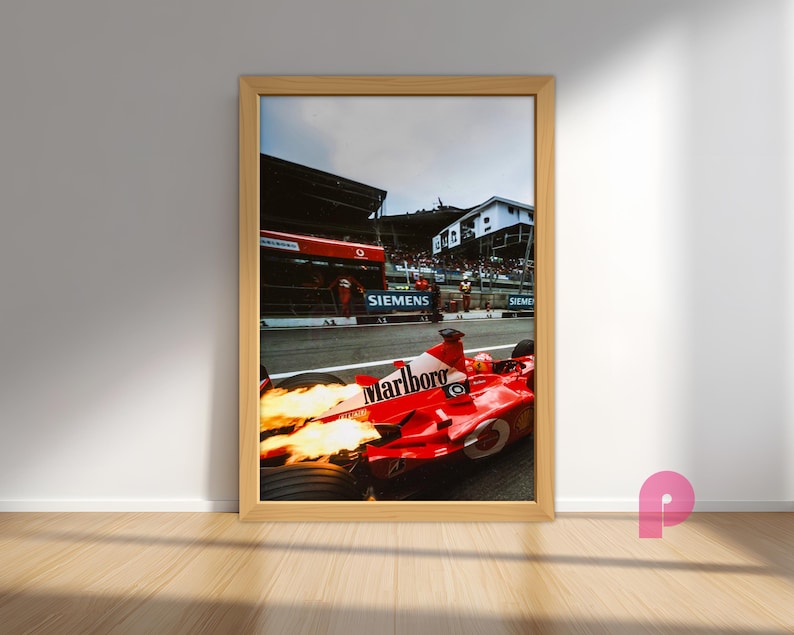 May include: Framed print of a red Formula 1 race car with the Marlboro logo, flames emitting from the exhaust. The car is on a racetrack with the Siemens logo visible. The image is in a wooden frame.