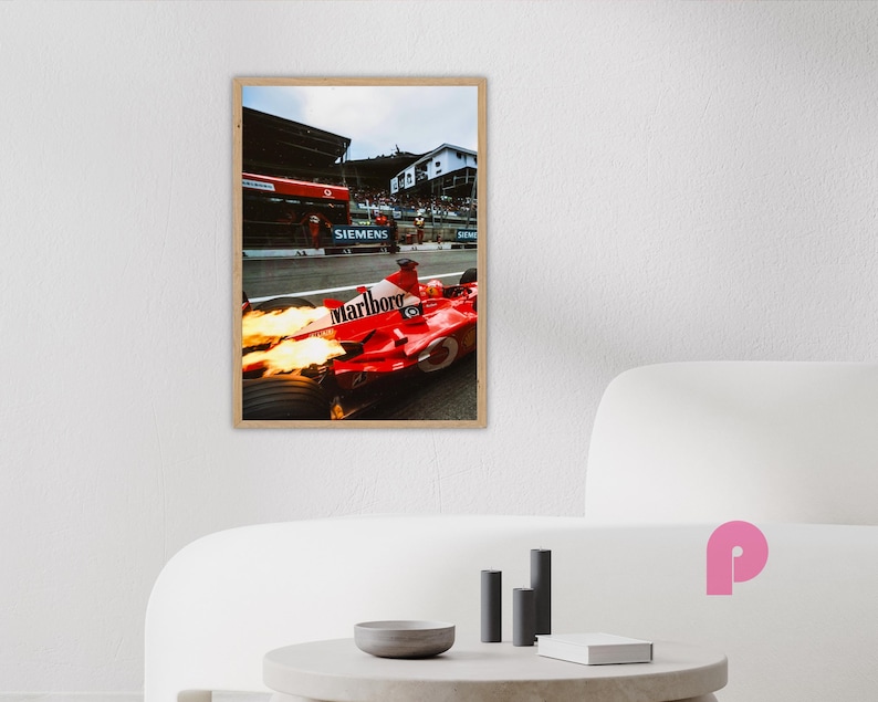 May include: A framed print of a red Formula 1 race car with the Marlboro logo, flames erupting from the exhaust. The image captures the car in motion on a racetrack, with a backdrop of buildings and spectators. The print is in a wooden frame.