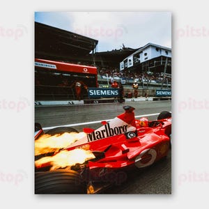 May include: A Formula 1 race car in motion, with flames erupting from the exhaust. The car is red with white and black branding, including "Marlboro." The scene includes a pit area and spectators, capturing the energy of a race.