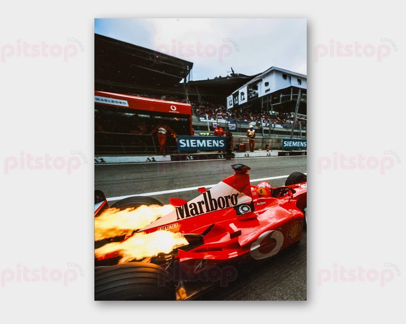 May include: A Formula 1 race car in motion, with flames erupting from the exhaust. The car is red with white and black branding, including "Marlboro." The scene includes a pit area and spectators, capturing the energy of a race.