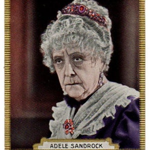 Könnte beinhalten: Ein Schwarzweißfoto einer älteren Frau mit grauem Haar. Sie trägt ein violettes Kleid mit einem weißen Spitzenkragen und ein Diadem mit Schmucksteinen. Der Text "ADELE SANDROCK" ist unter dem Foto gedruckt.