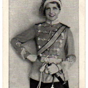 May include: Vintage black and white trading card featuring Mady Christians. She is wearing a military-style jacket with multiple buttons, a sash, and a decorative hat. The card has a white border and the name "Mady Christians" at the bottom.