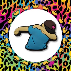 May include: A blue and black rubber figurine of a person doing the "dab" dance pose. The person is wearing a blue shirt and a black hat with a pink heart on it.