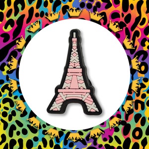 May include: A pink and white Eiffel Tower charm with a black outline. The charm is made of a soft, pliable material and is ideal for adding a touch of Parisian flair to your jewellery or crafts.
