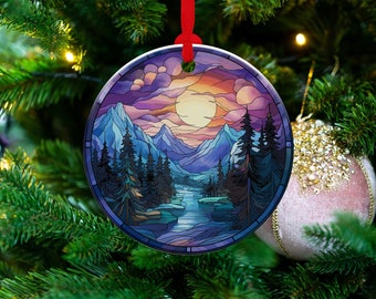May include: A round Christmas ornament with a stained glass design of a mountain landscape. The scene features a purple and blue sky with a bright yellow sun, a river winding through a forest, and a mountain range in the background.