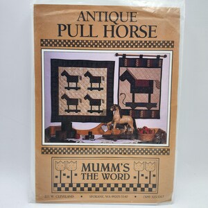Pode incluir: Uma embalagem de papel castanho com o texto "ANTIQUE PULL HORSE" e "MUMM'S THE WORD". A embalagem apresenta imagens de colchas com temas de cavalos e uma pequena estatueta de cavalo. A embalagem é selada em plástico transparente.