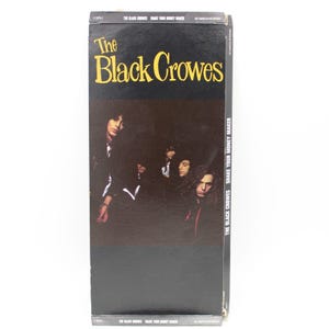 May include: A black and white album cover for "Shake Your Money Maker" by The Black Crowes. The album title is in large yellow letters above a band photo. The band members are in a dark setting.