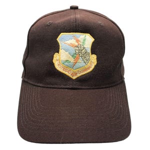 May include: A white ceramic mug with a black handle and the text "But First, Coffee" in a bold, black font. The mug is set against a blurred background, suggesting a cosy setting.