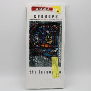 Może przedstawiać: Zapieczętowana płyta CD z albumem "The Innocents" zespołu Erasure. Okładka albumu przedstawia ilustrację w stylu witrażu z postaciami w kolorze niebieskim, żółtym i brązowym. Opakowanie zawiera naklejkę "Super Saver" i metkę z ceną.