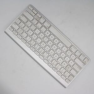 May include: A silver-colored wireless keyboard with white keys. The keyboard has a standard QWERTY layout with numbers and symbols. The keys are rectangular and slightly rounded. The keyboard is angled slightly.