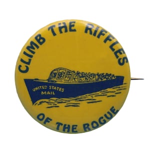 May include: Yellow button with blue text and a boat illustration. The text reads "CLIMB THE RIFFLES OF THE ROGUE" with "UNITED STATES MAIL" on the boat. A pin is attached to the back.