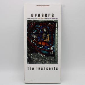 Może przedstawiać: Pudełko na płytę CD z albumem "The Innocents" zespołu Erasure. Okładka przedstawia ilustrację w stylu witrażu z postaciami w otoczeniu kościelnym. Nazwa zespołu i tytuł albumu są czarne, z logo CompactDisc u góry. Zawiera dwa dodatkowe utwory.