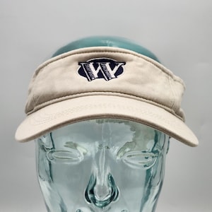 Puede incluir: Una visera beige con una visera curvada. La visera presenta un logotipo azul marino bordado con las letras "WW" dentro de un borde azul marino. Se muestra en una cabeza de cristal transparente.