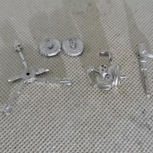May include: A set of silver metal model parts for a gun turret. The set includes two round wheels, a gun barrel, and a base with a rotating mechanism.