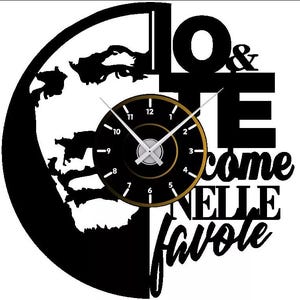Puede incluir: Un reloj de pared negro y dorado con el texto "IO & TE come NELLE favole". La esfera del reloj es negra con ribete dorado y manecillas blancas. El reloj está sobre una silueta negra de un mapa.