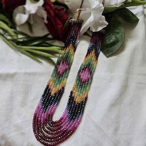 Puede incluir: Un collar de múltiples hilos hecho de cuentas de piedras preciosas de colores. El collar presenta un patrón geométrico con cuentas rosas, verdes, azules y amarillas. El collar está hecho de múltiples hilos de cuentas, creando un efecto de capas.